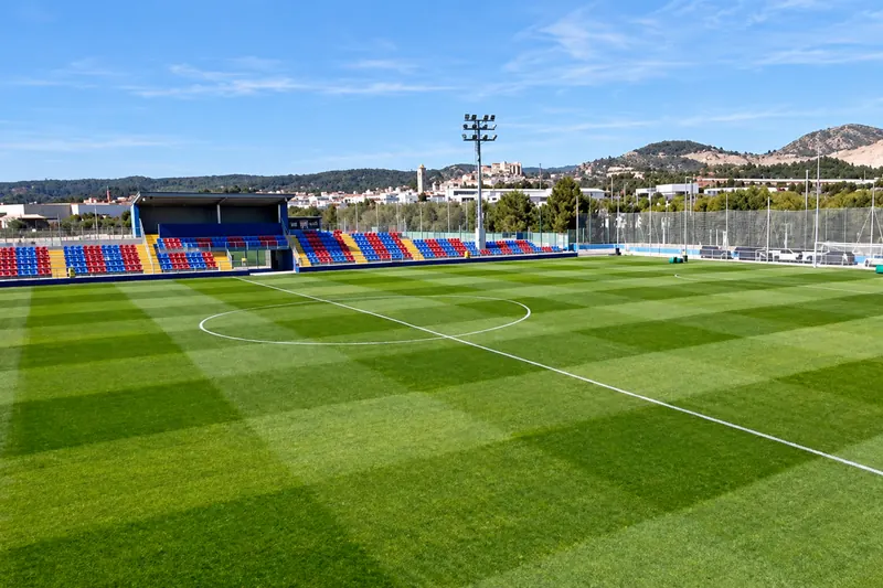 The mini-stadium at the Levante UD training ground, with its blue and claret stand and the Buñol mountains behind