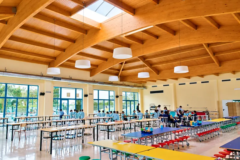 Dining hall with a wooden ceiling, long tables and large windows